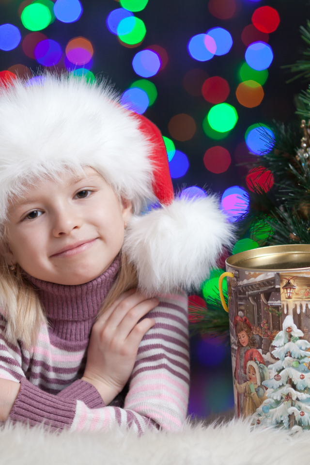 Маленькая девочка в новогодней шапке у елки