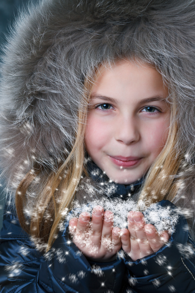 Маленькая девочка в капюшоне сдувает снежинки с ладоней
