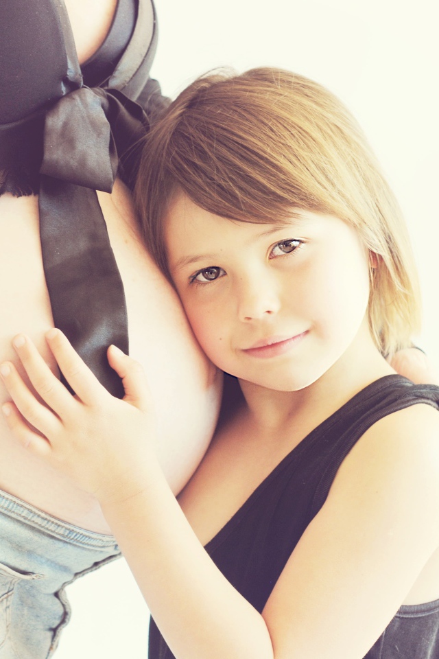 Маленькая девочка прислоняется к животу беременной женщины