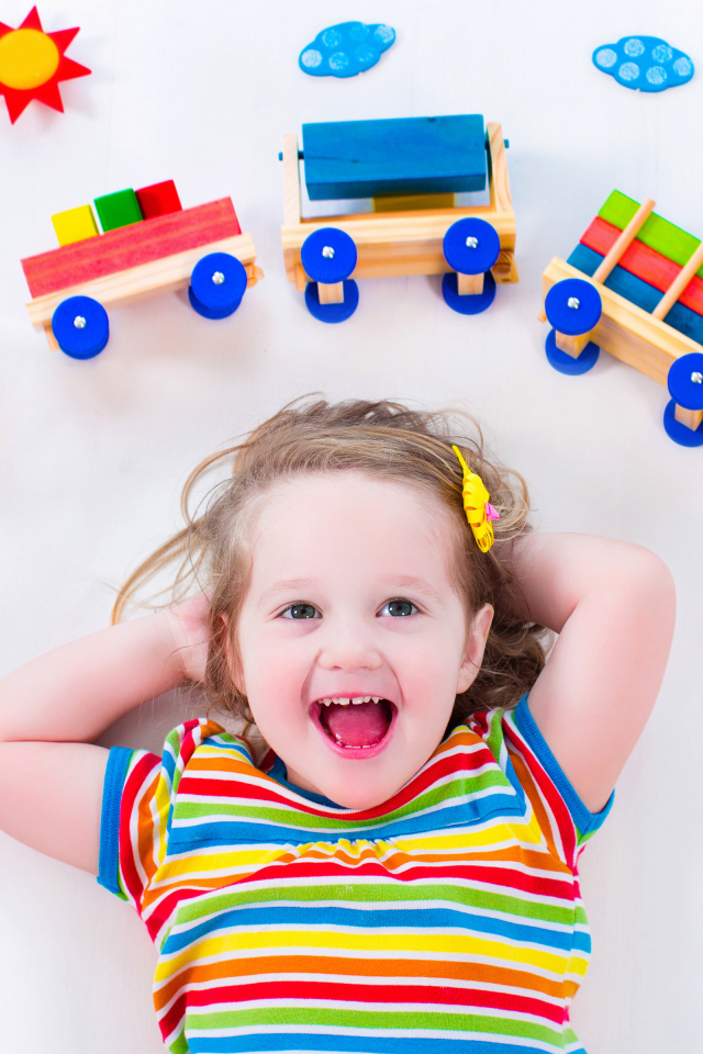 Маленькая девочка на сером фоне с игрушечным паровозом 