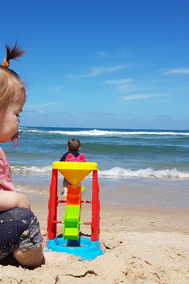 Маленькая девочка играет на песке у моря