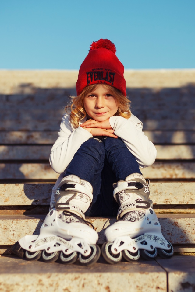 Маленькая девочка в роликах сидит на ступеньках 