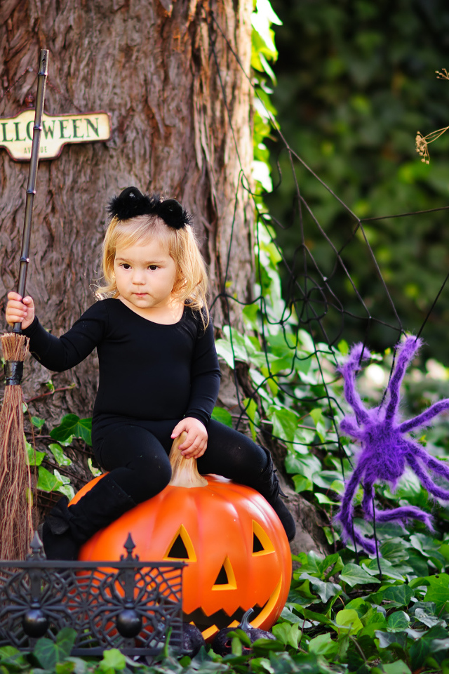 Маленькая девочка сидит на тыкве в лесу в костюме на Хэллоуин 