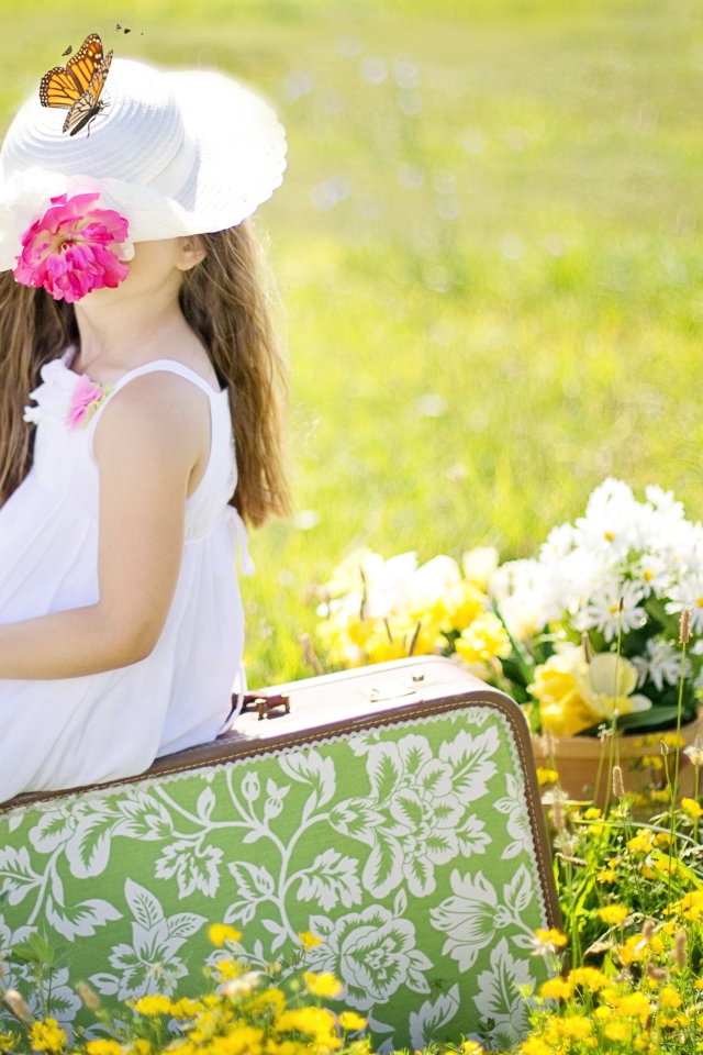 Маленькая девочка сидит на чемодане на поле с цветами