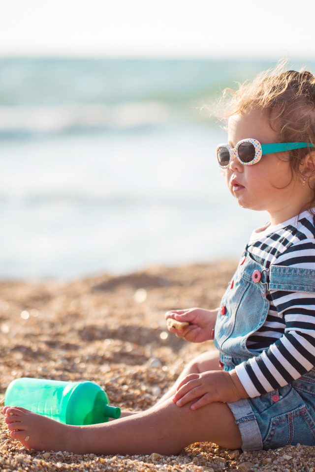 Маленькая девочка сидит на песке на пляже