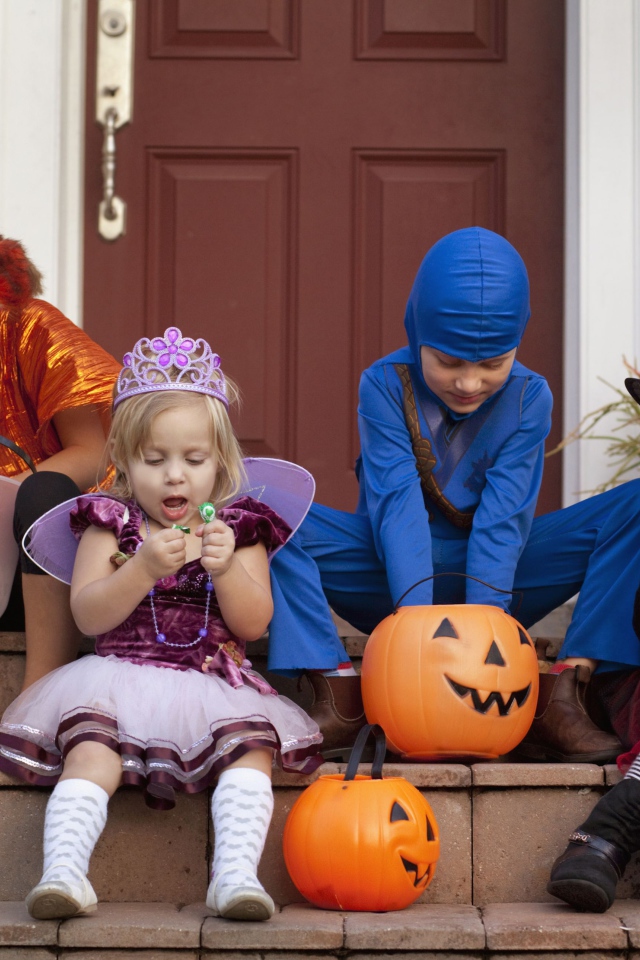 Маленькие дети в костюмах на Хэллоуин сидят на ступеньках со сладостями