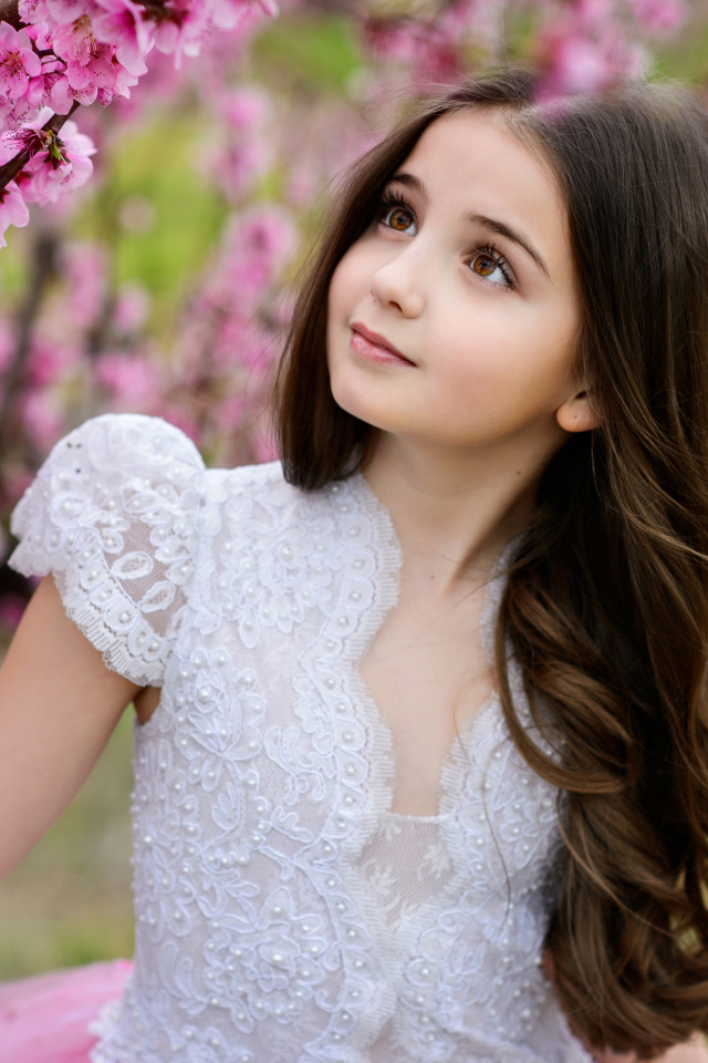 Маленькая длинноволосая девочка у дерева с розовыми цветами