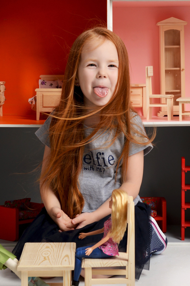 Маленькая длинноволосая девочка показывает язык