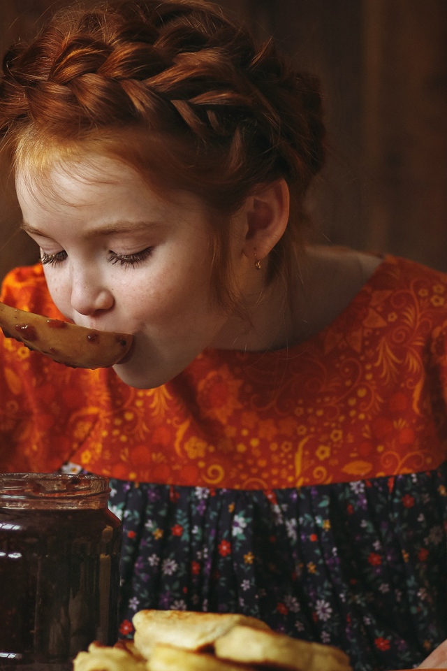 Маленькая рыжеволосая девочка пробует варенье