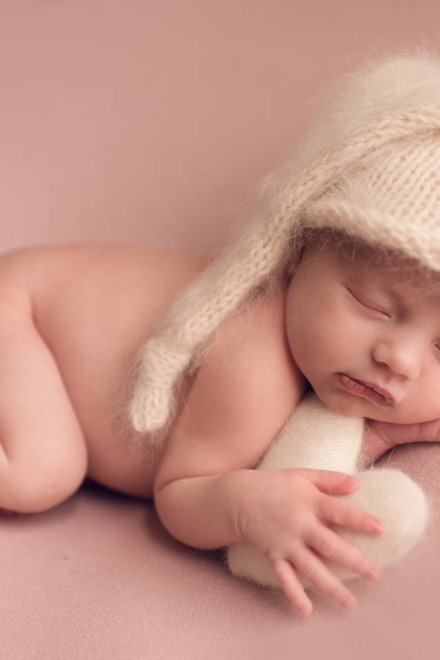 Маленький спящий ребенок в теплой шапке на розовом фоне