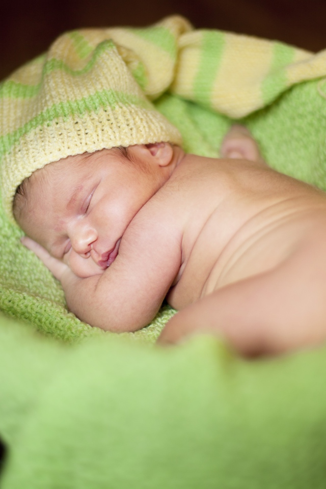 Маленький спящий грудной ребенок на зеленом покрывале 