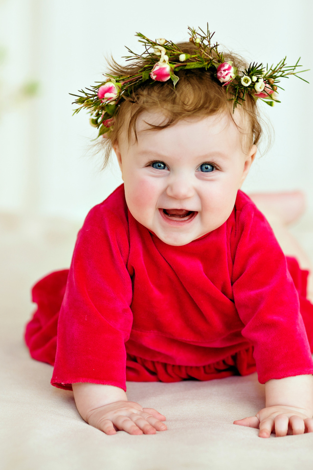 Маленькая улыбающаяся девочка в красном платье с венком на голове