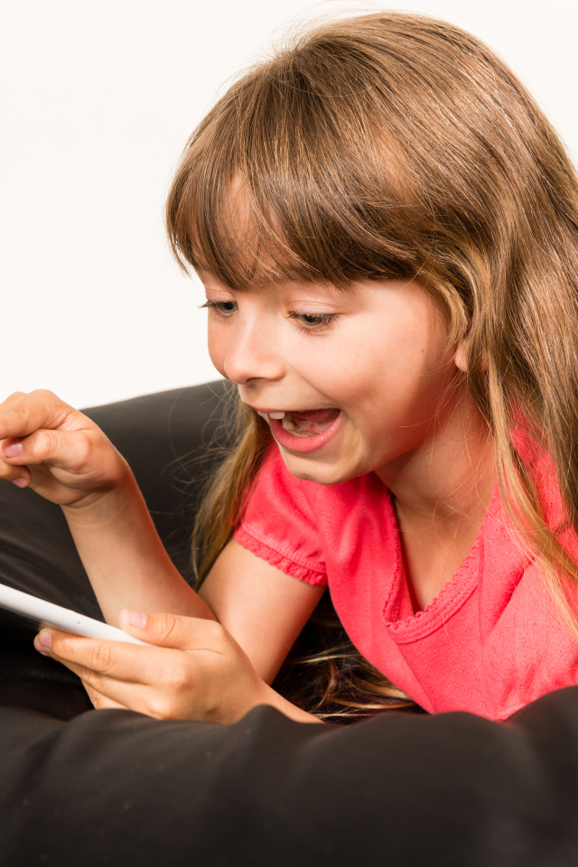 Маленькая улыбающаяся девочка лежит с планшетом