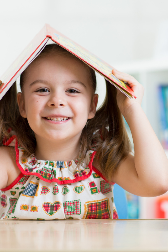 Маленькая улыбающаяся девочка с книгой на голове