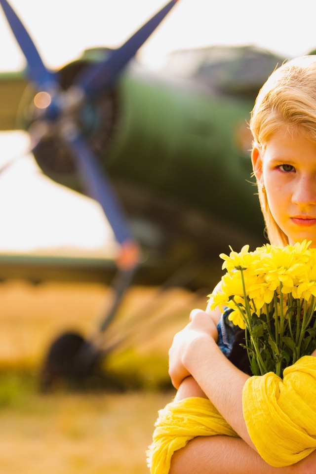 Длинноволосая девочка с букетом желтых хризантем на фоне самолета 