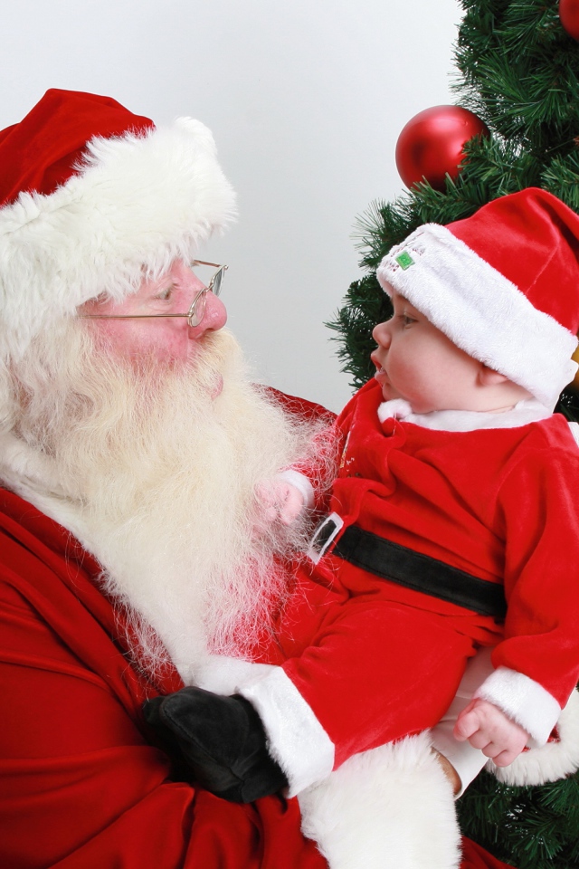 Дед Мороз держит на руках маленького ребенка у елки