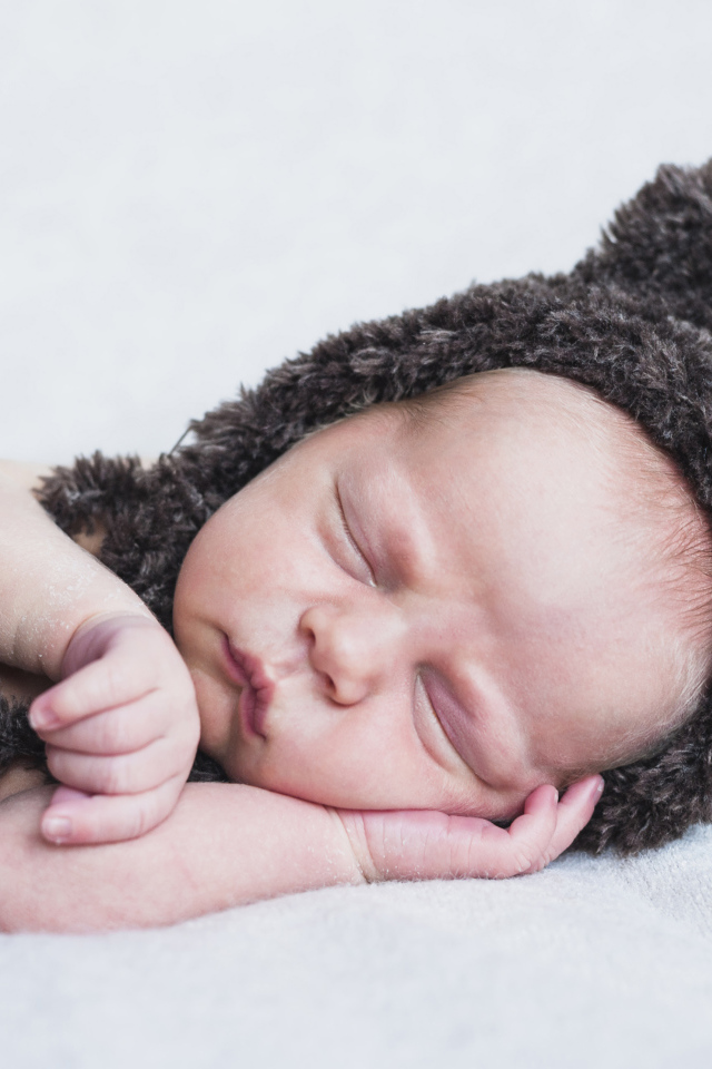 Спящий грудной ребенок в меховой шапке