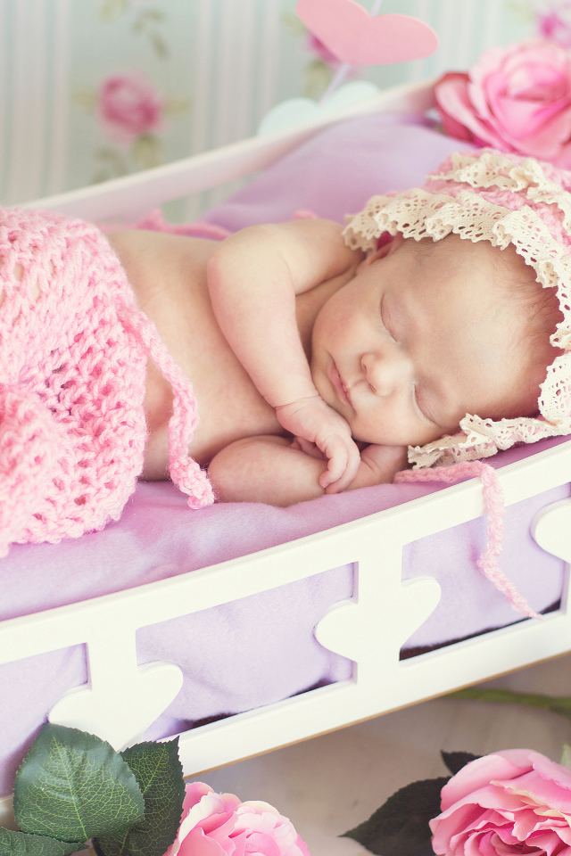 Спящий ребенок в розовом вязаном костюме в колыбели
