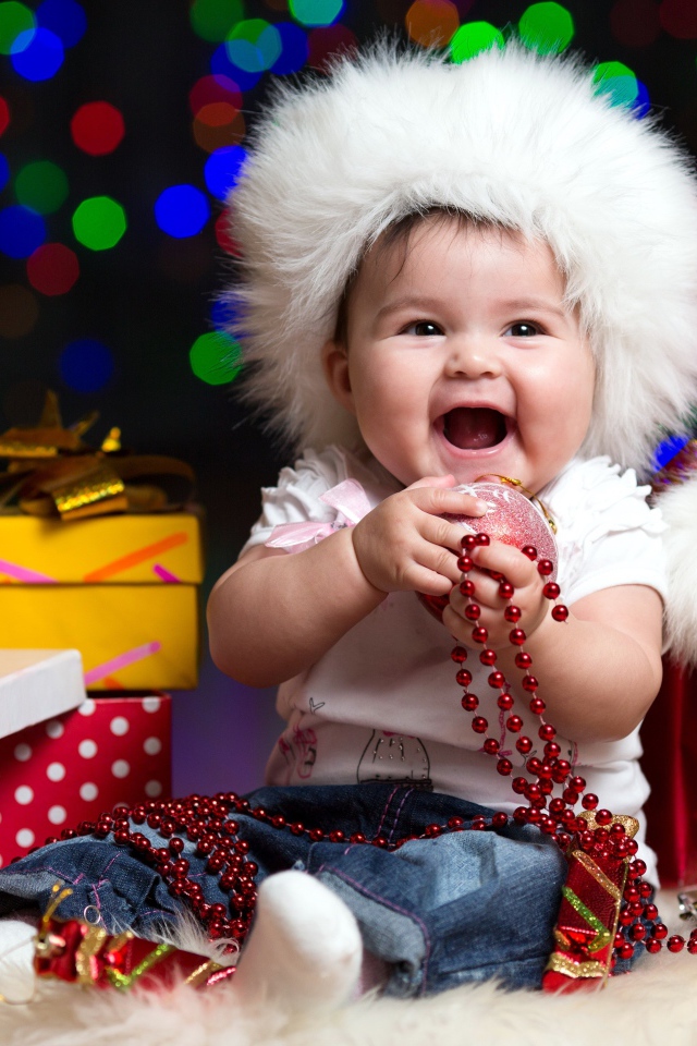 Улыбающийся малыш в новогодней шапке с подарками у елки