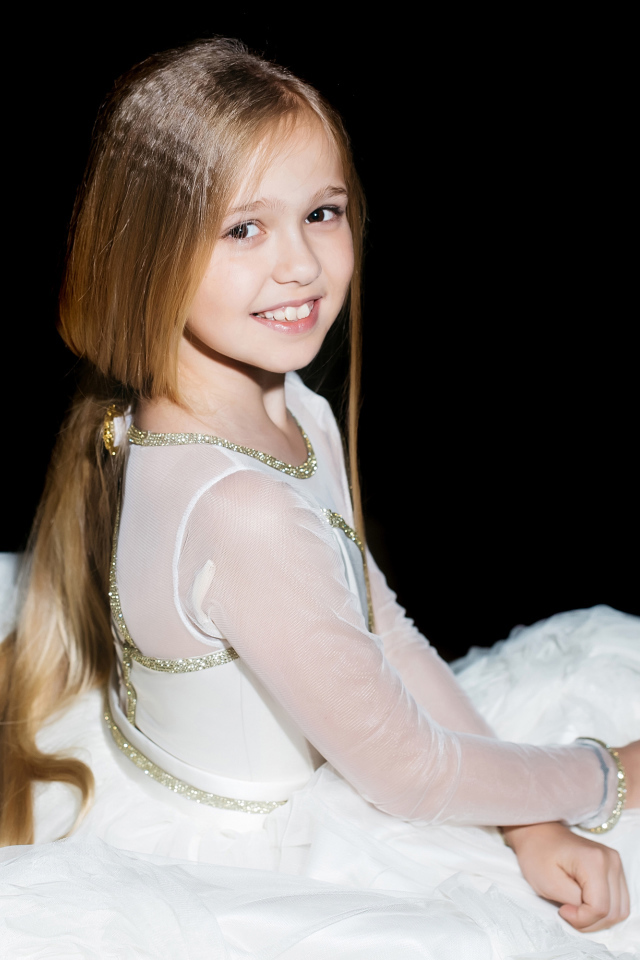 Улыбающаяся девочка в красивом белом платье на черном фоне