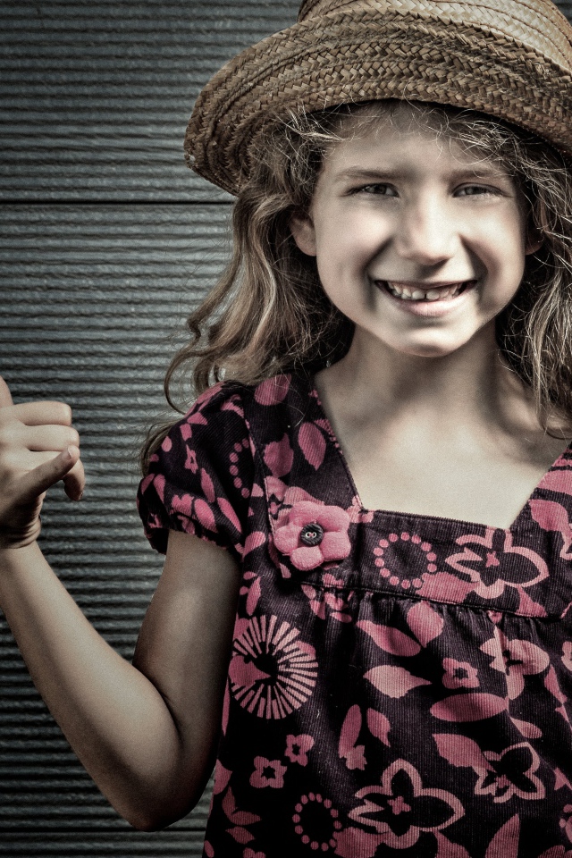 Улыбающаяся девочка в соломенной шляпе у стены 