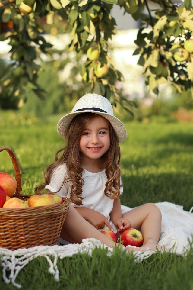 Улыбающаяся девочка сидит на зеленой траве с яблоками