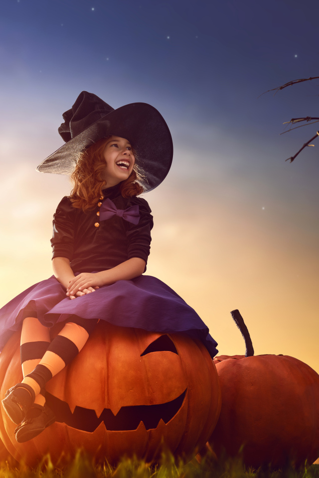 Улыбающаяся девочка сидит на тыкве в костюме на Хэллоуин 