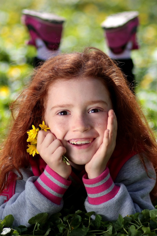 Улыбающаяся рыжеволосая девочка лежит на зеленой траве