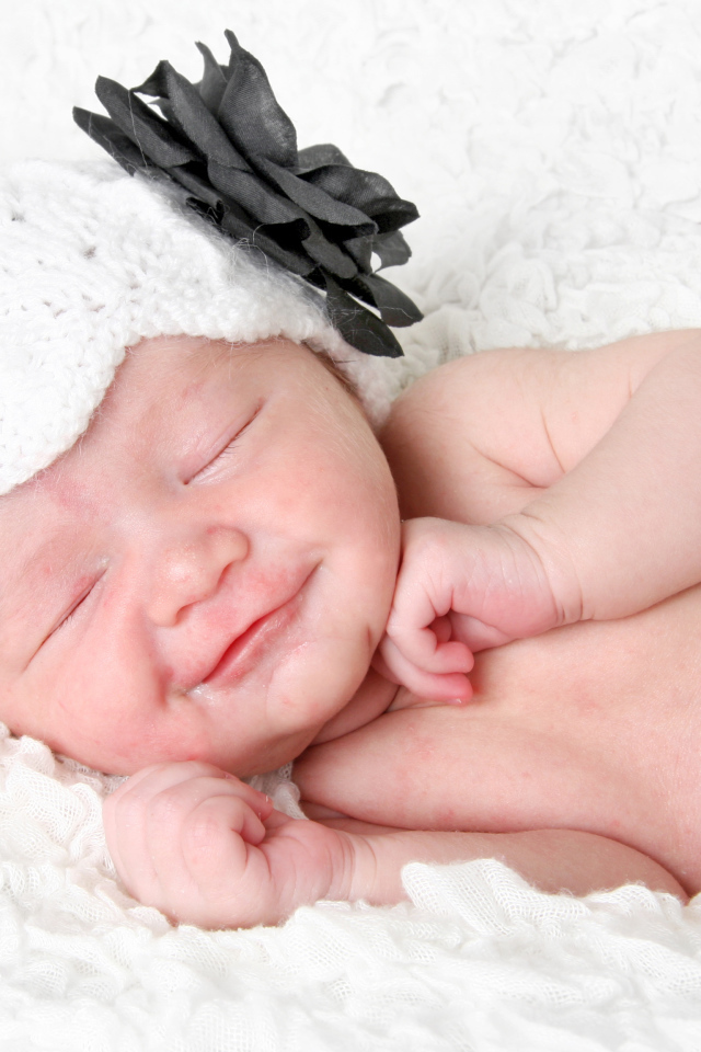 Улыбающийся спящий ребенок в белой вязаной шапке с цветком