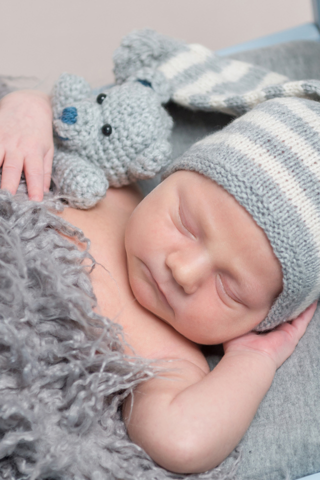 Младенец в вязаной шапке спит с игрушкой под меховым одеялом