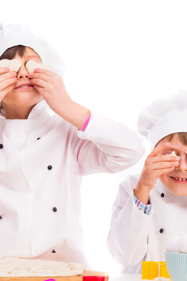 Два маленьких мальчика в костюмах повара на кухне делают печенье