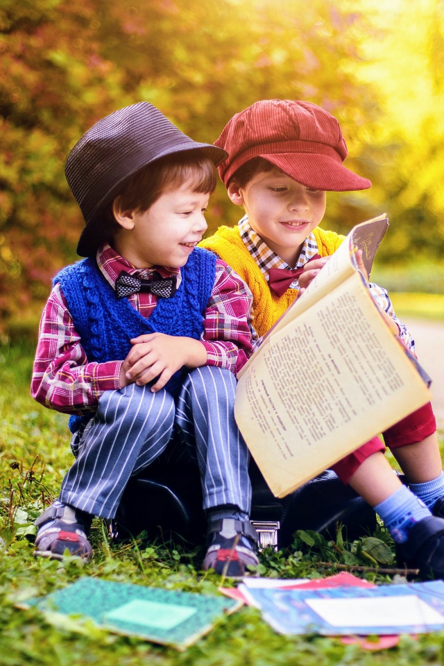 Два маленьких мальчика читают книгу сидя на траве