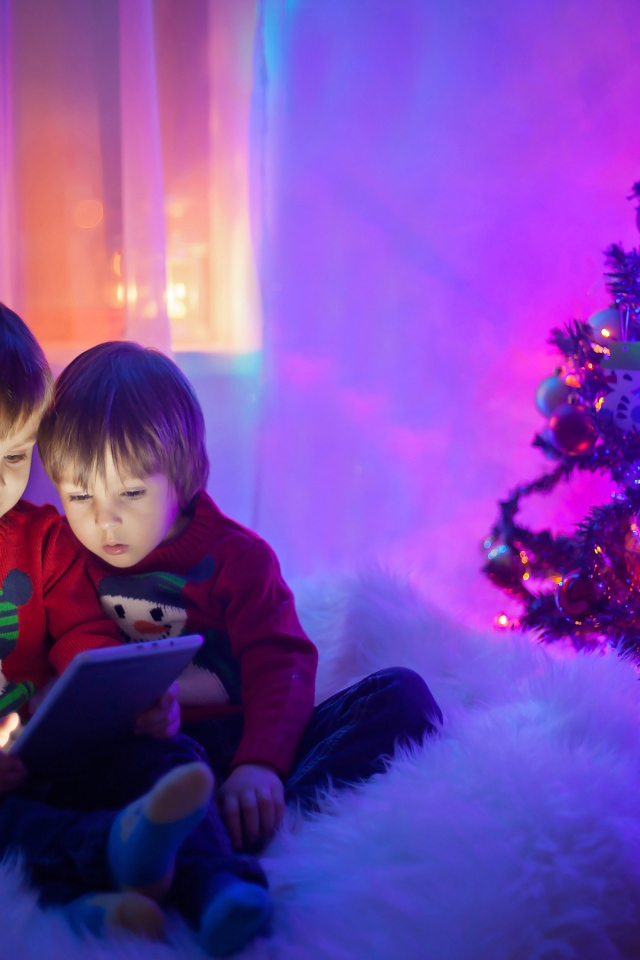 Два маленьких мальчика смотрят мультики у новогодней елки