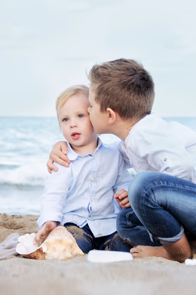 Два маленьких брата сидят на песке на пляже