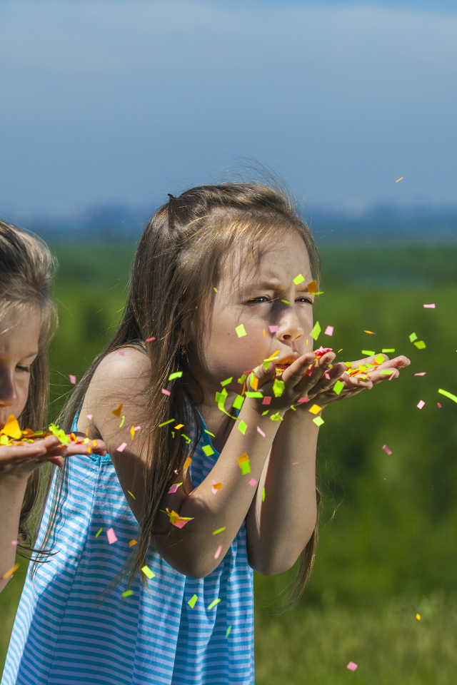 Две маленькие девочки сдувают конфетти  с рук