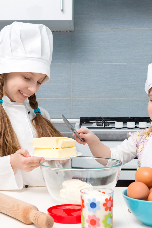 Две маленькие девочки в костюмах повара готовят на кухне