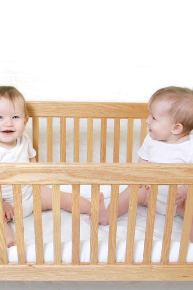 Два улыбающихся малыша в деревянной кроватке