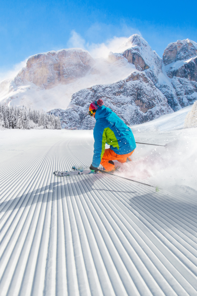 Лыжник спускается по склону на фоне заснеженных гор 