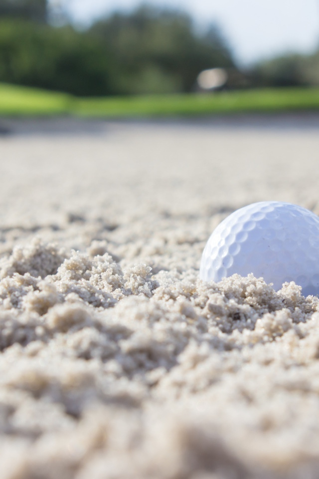 Белый мяч для гольфа лежит на песке