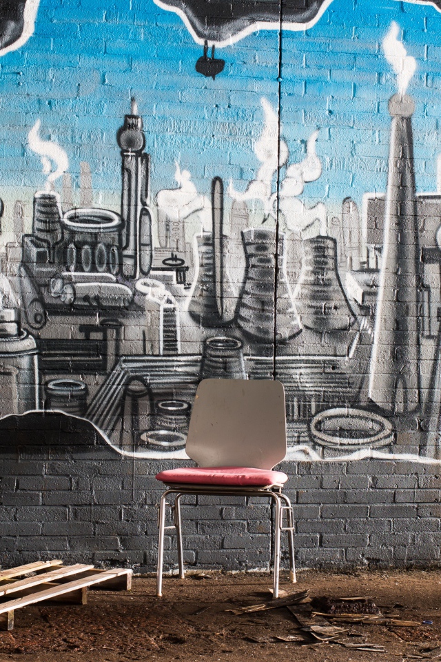 A chair stands by a brick wall with graffiti