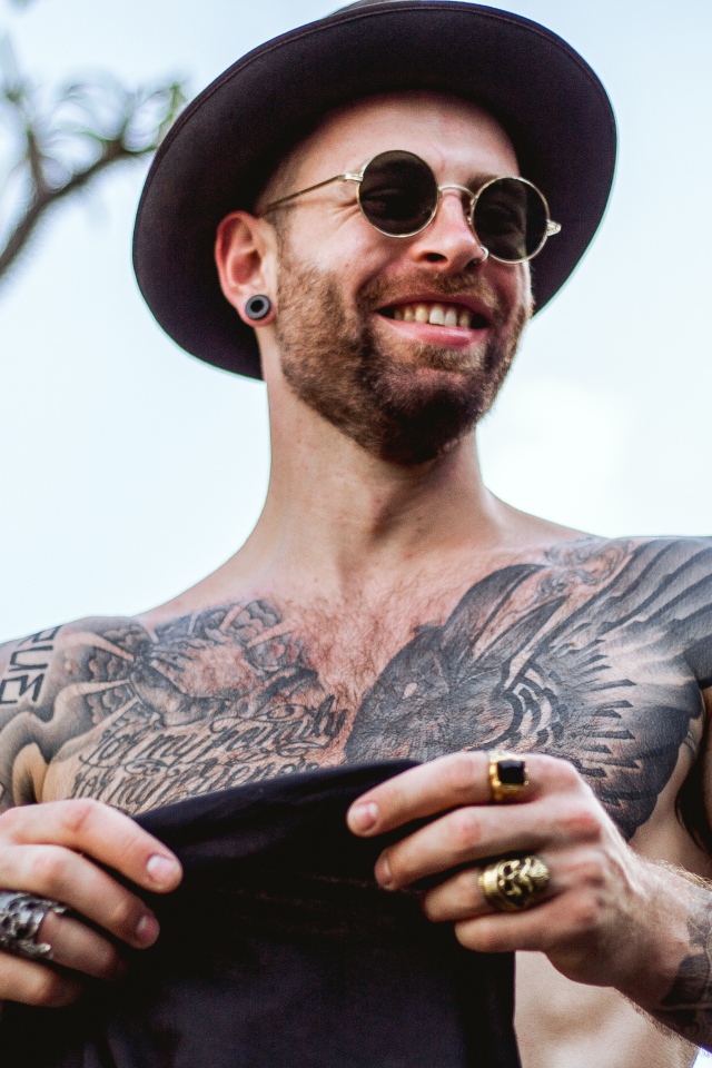 A man with tattoos on his body in a black hat and glasses