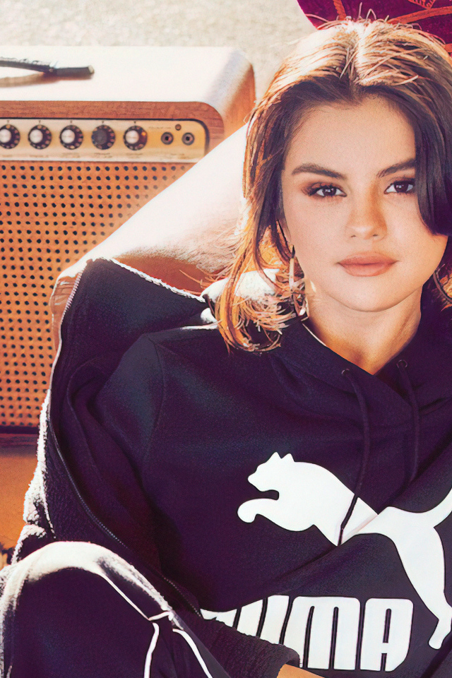 Актриса Селена Гомес в спортивном костюме сидит на полу у дивана