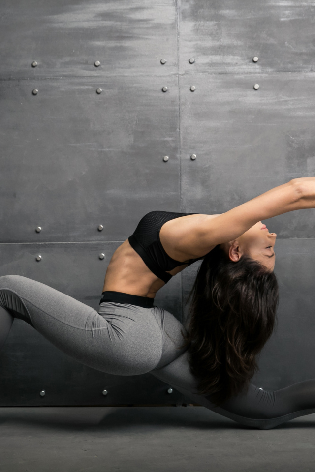 Спортивная девушка занимается гимнастикой на фоне серой стены
