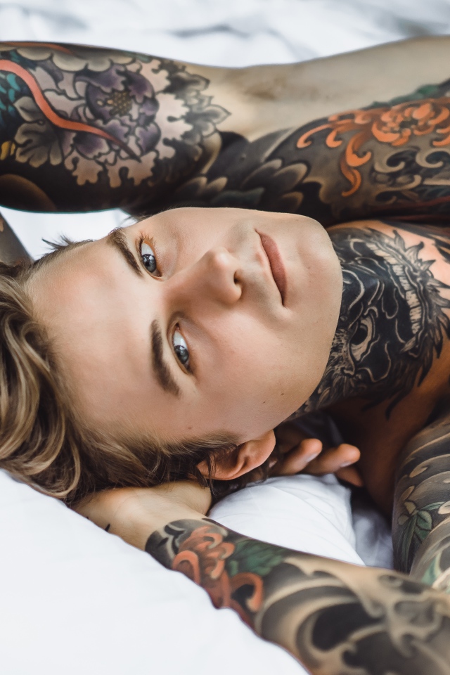 Handsome young man with tattoos on his body is lying on the bed