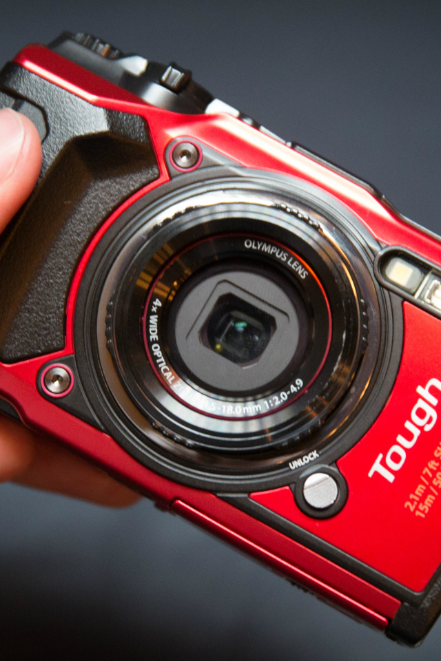 Красный фотоаппарат Olympus Tough TG-5 в руке на сером фоне