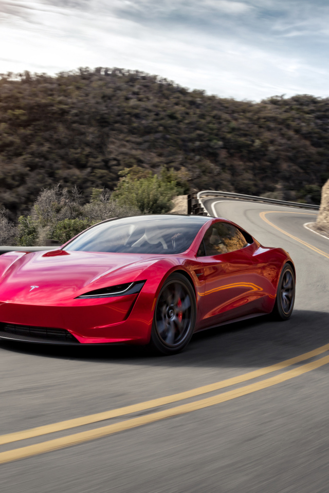 Красный автомобиль Tesla Roadster на трассе у гор 