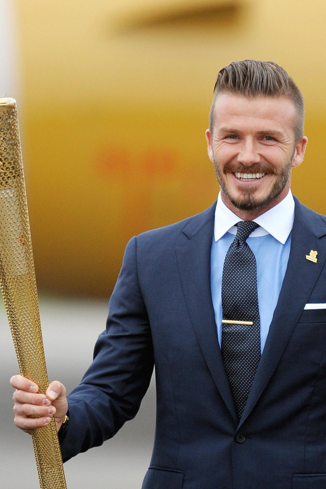 Улыбающийся футболист Дэвид Бекхэм с олимпийский огнем в руке