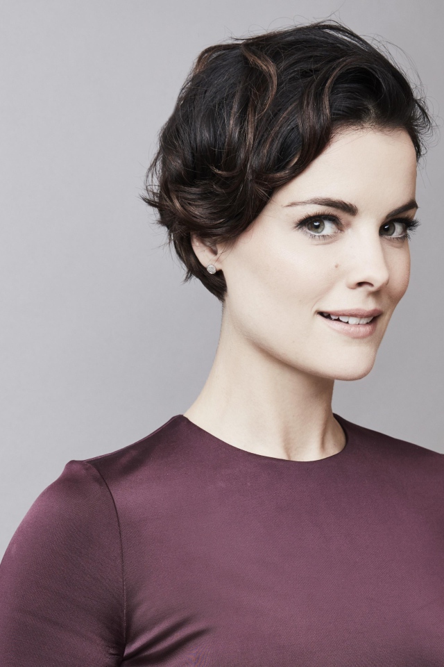 Улыбающаяся девушка, актриса Джейми Александр на сером фоне