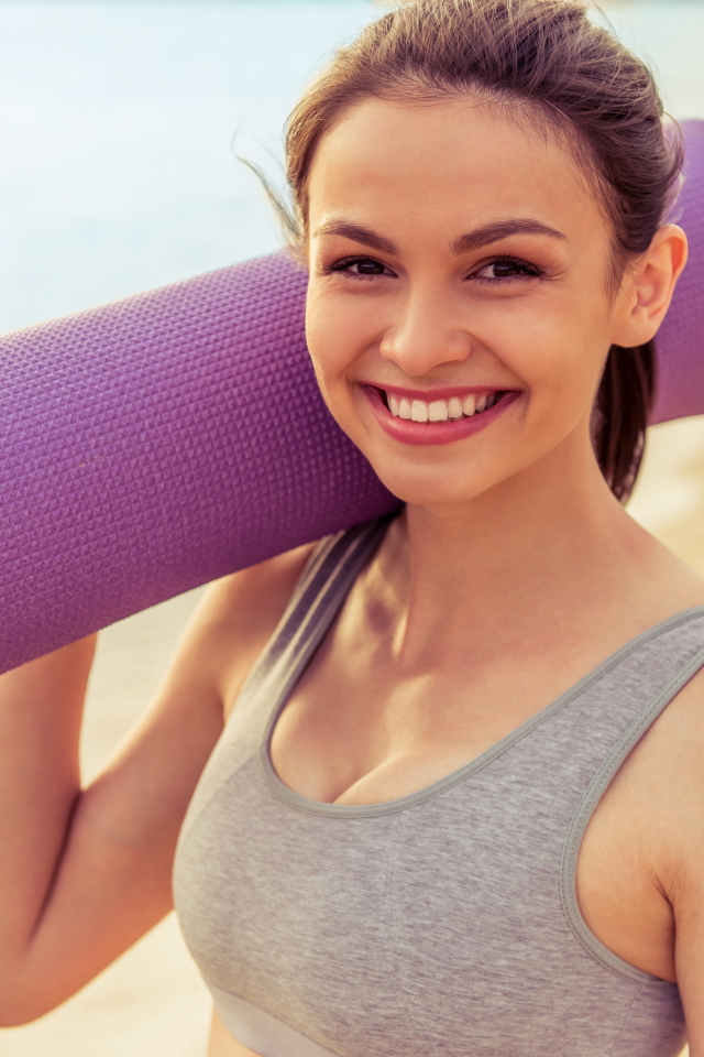 Спортивная девушка с ковриком для йоги на пляже