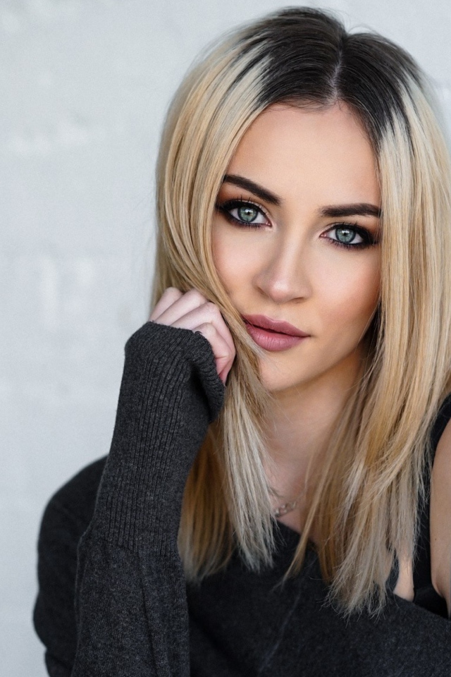 Стильная блондинка с татуировкой на плече на фоне стены